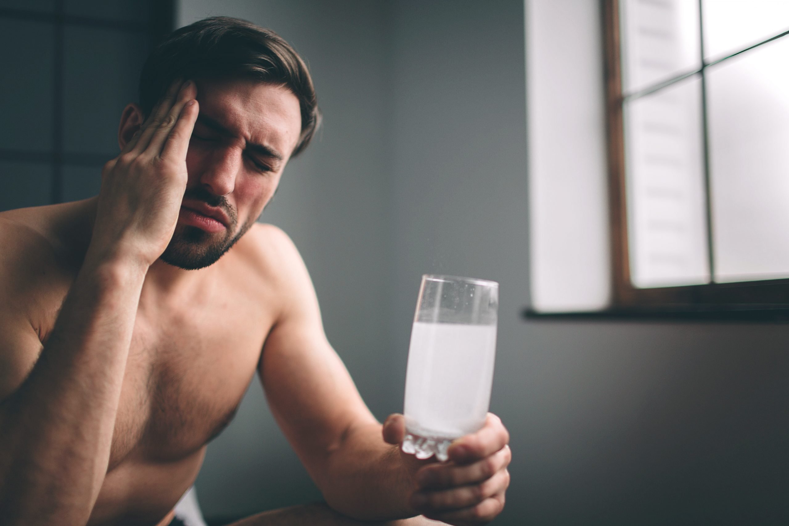 Jak pozbyć się kaca? Mężczyzna na kacu trzyma w ręku szklankę z musującą aspiryną