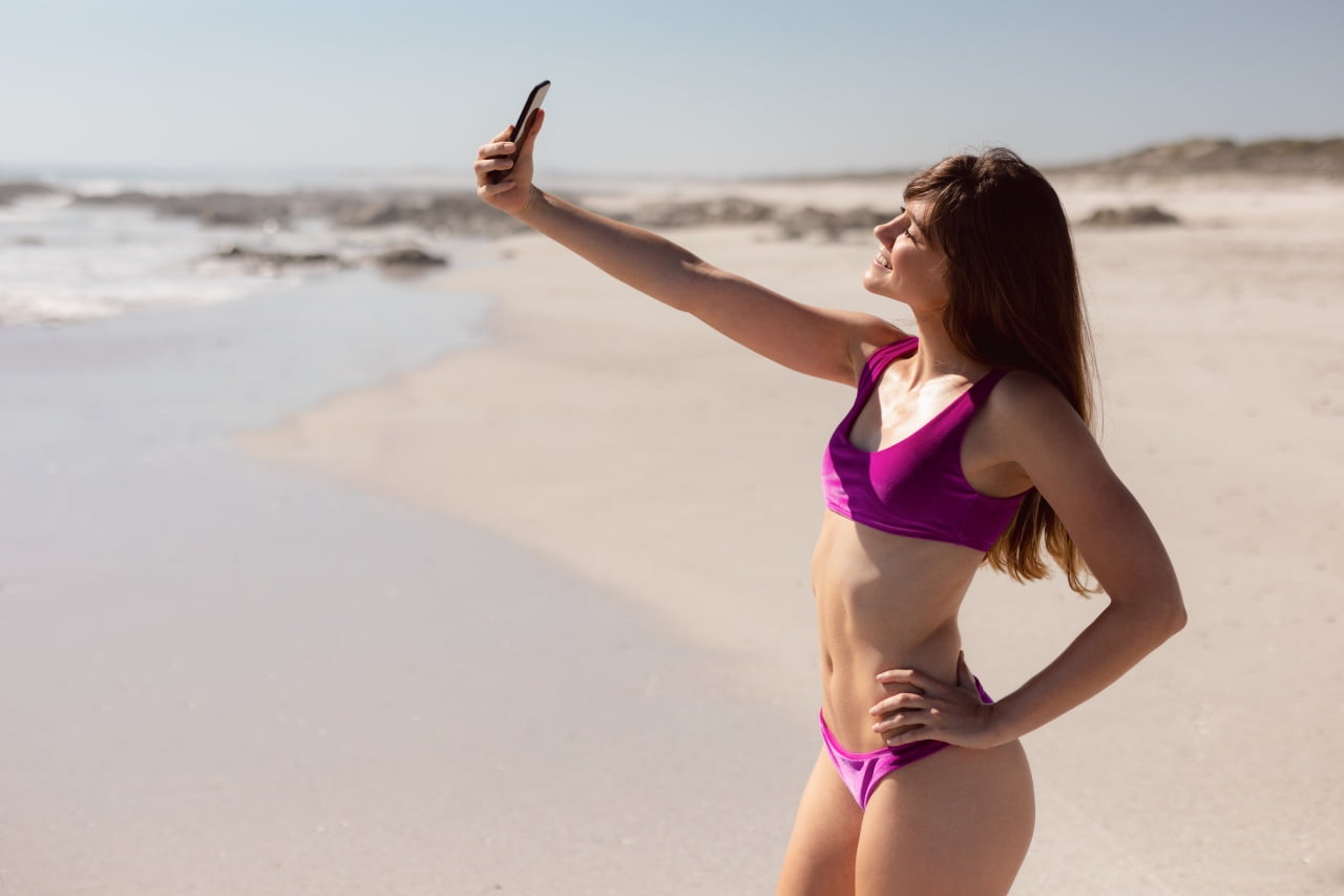 Jak zadbać o telefon w upalne dni. Młoda kobieta robi selfie na plaży