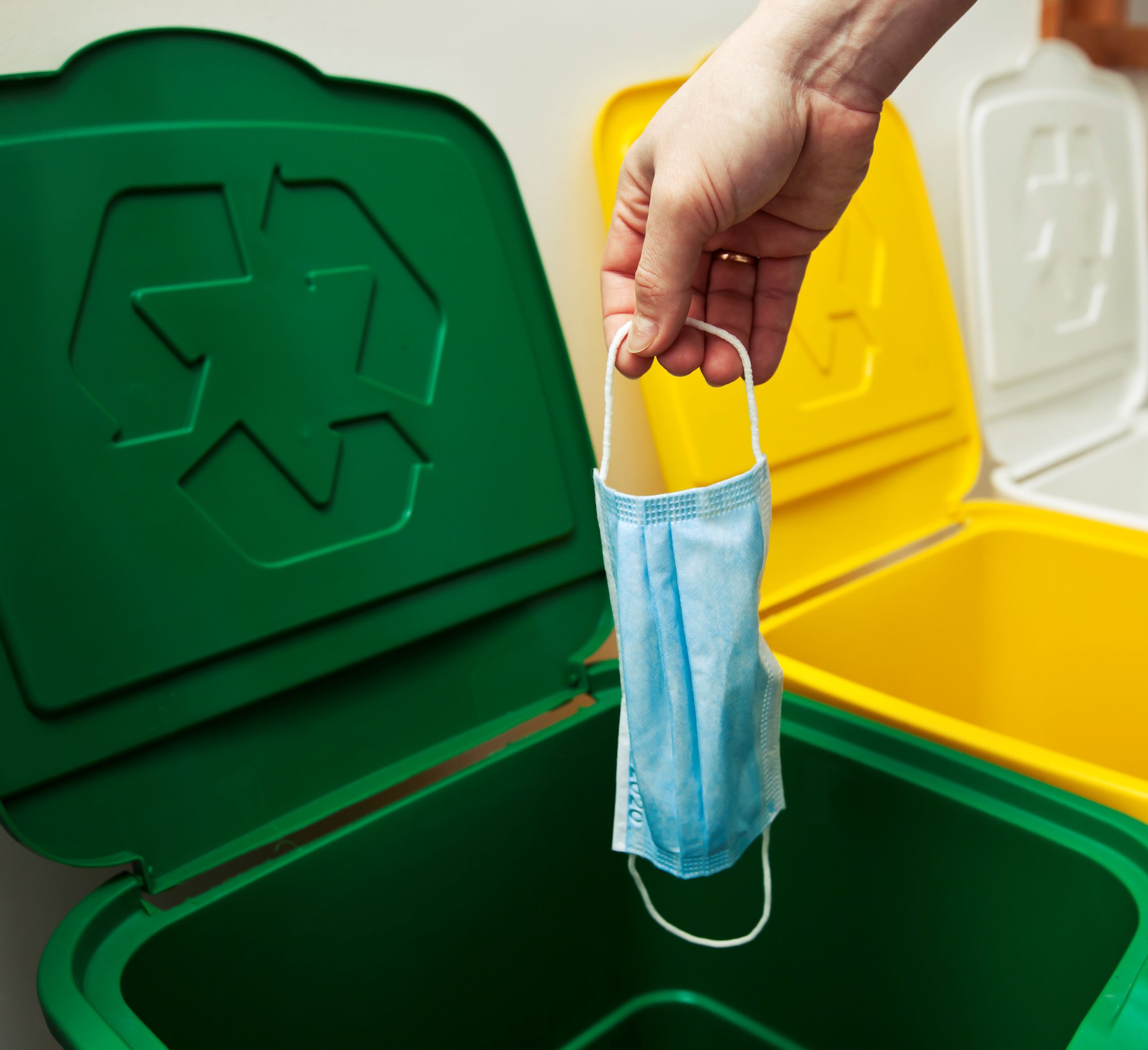 Kobieta wyrzuca zużytą maseczkę do zielonego kosza z odpadami do recyklingu